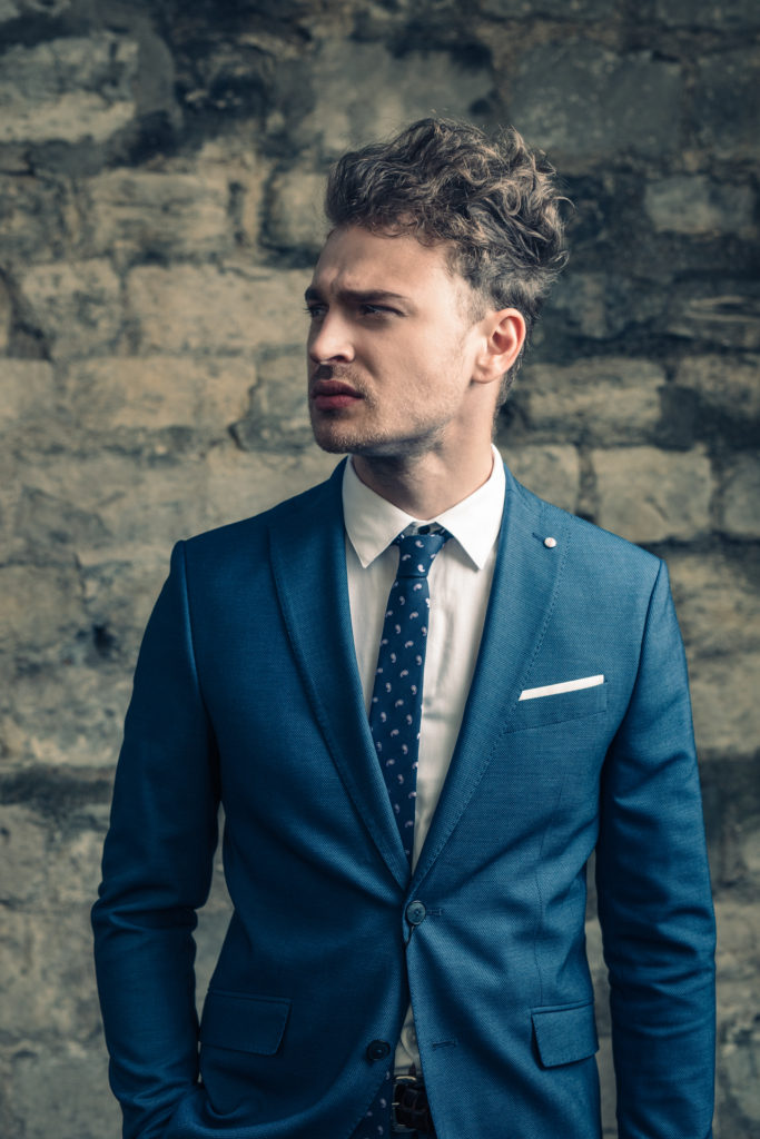 Men wearing blue suit standing in front of brick wall